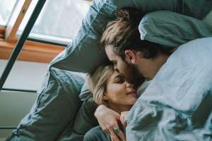 ベッドの中で男性が女性のおでこにキスをしている